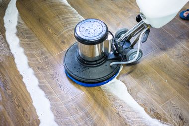 Mit einer Bodenpoliermaschine wird ein Hartholzboden gereinigt, wobei eine Spur aus Seifenwasser entsteht.